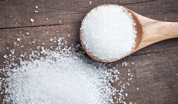 A wooden spoon filled with Organic Erythritol Sweetener is placed on a wooden surface, with more Organic Erythritol Sweetener beside it.